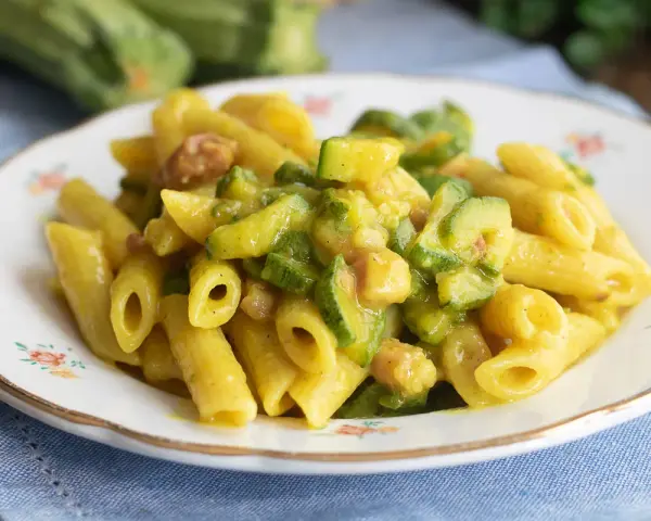 Piatto di pasta penne con zucchine a rondelle e cubetti di pancetta croccante, condita con una salsa cremosa.
