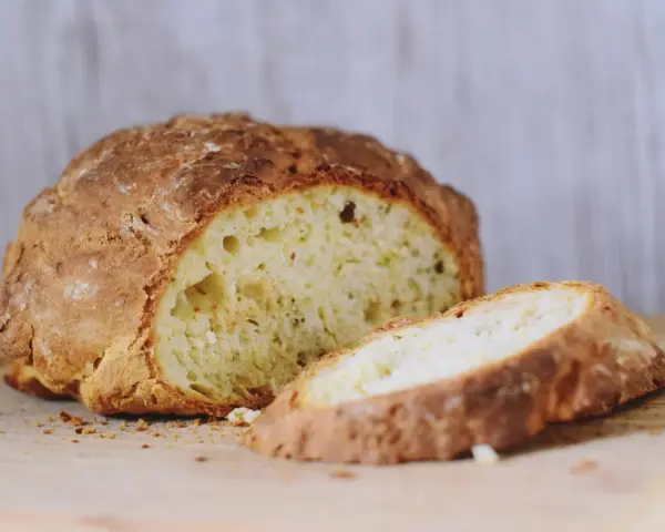 Chrupiący, złocisty bochenek soda bread, z jednym plastrem odciętym, na drewnianej desce.
