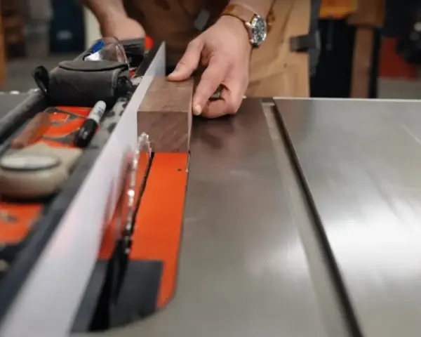 Hands guide a wooden plank along a table saw's fence, demonstrating how to use a table saw for precise cuts.