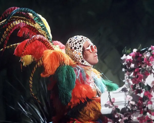 Elton John in einem extravaganten Federkostüm, das an einen Pfau erinnert. Seine ikonischen Elton John Outfits sind legendär.