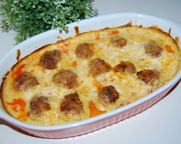 Pulpety w sosie śmietanowo-serowym, zapieczone w naczyniu, z zieloną dekoracją w tle.