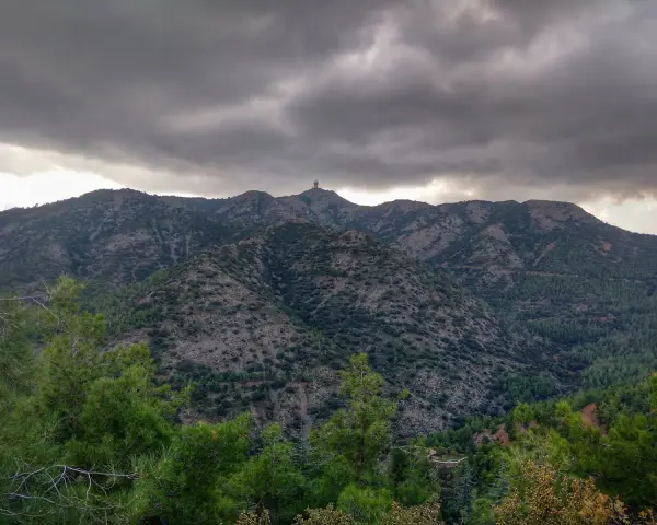Góry Troodos pod burzliwym niebem. W oddali na szczycie widać charakterystyczną budowlę.