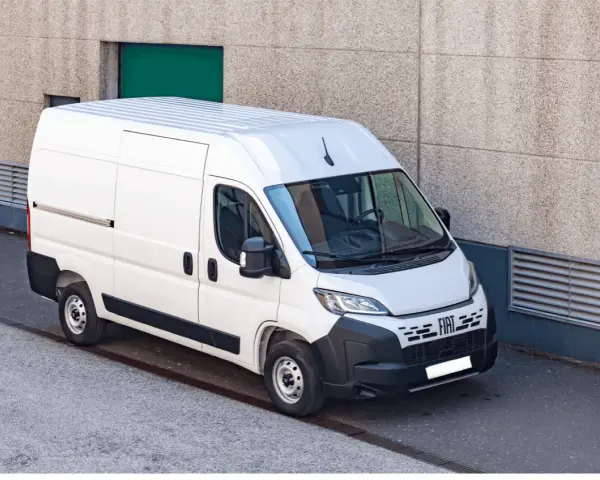 Biały bus dostawczy Fiat Ducato zaparkowany przy betonowej ścianie budynku.