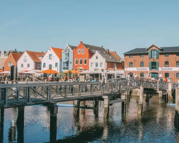 Bunte Häuser am Hafen, ein Steg führt über das Wasser. Perfekt für Ausflüge in Husum, mit Cafés und dem alten Speicher.
