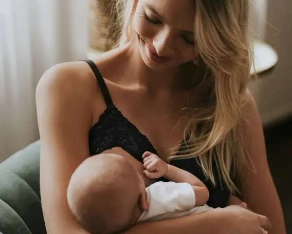 Uśmiechnięta mama karmi piersią swoje dziecko. Delikatne chwile bliskości i miłości.