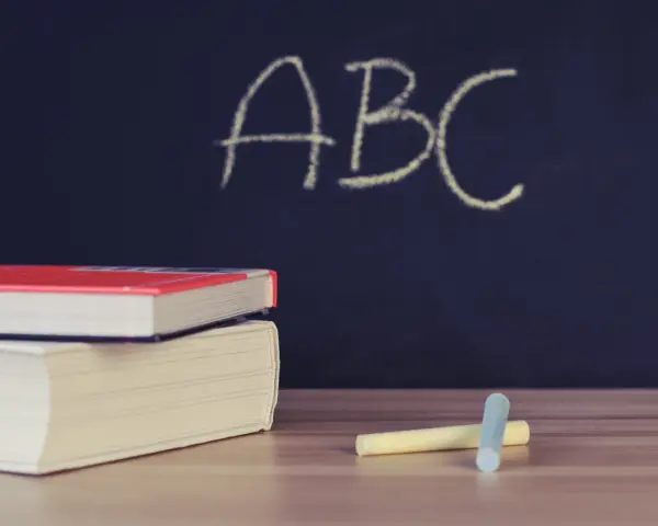 Libri e gessetti su un tavolo di legno, con la scritta "ABC" su una lavagna scura. Un'immagine che evoca l'inizio di nuovi percorsi di apprendimento, come i **corsi abilitanti**.