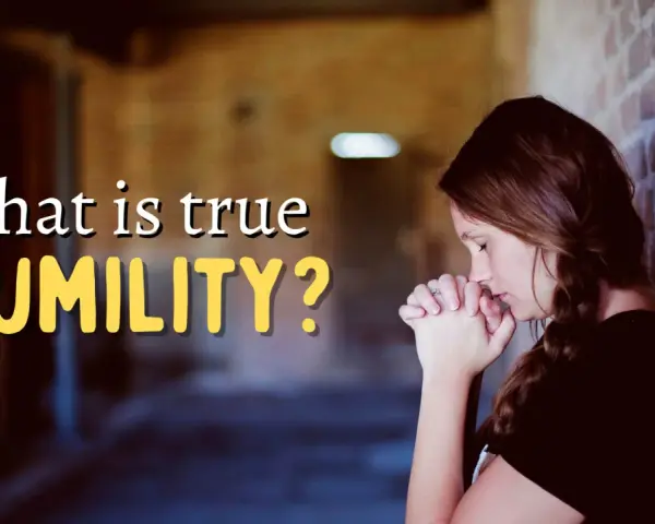 A woman with her hands clasped in prayer leans against a brick wall, contemplating "what is true HUMILITY?".