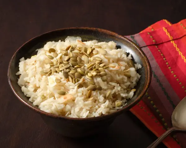 Un tazón de arroz de coco con semillas de calabaza y coco rallado, servido sobre una servilleta colorida.