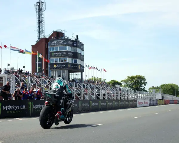 Motocyklista ściga się na wyspie Man, mijając trybuny pełne widzów i wieżę kontrolną.