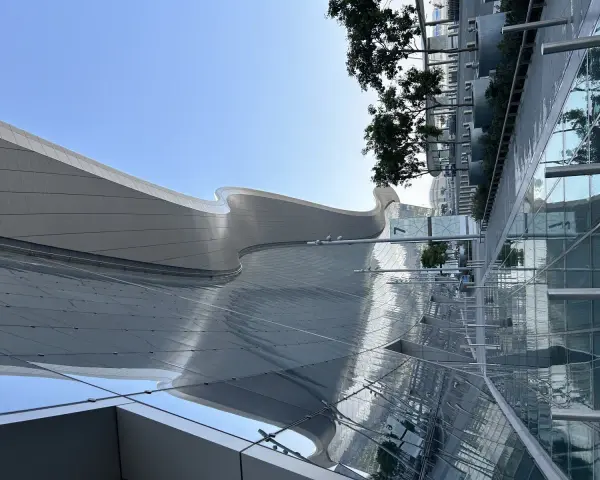 Nowoczesna architektura AUH Zayed International z falującym dachem i szklanymi fasadami odbijającymi niebo i zieleń.