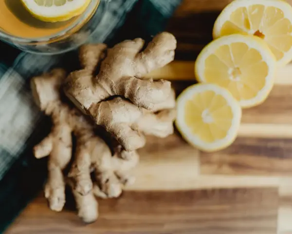 Un verre de thé avec une tranche de citron et du gingembre frais sur une planche en bois. Parfait pour boire du gingembre le matin.