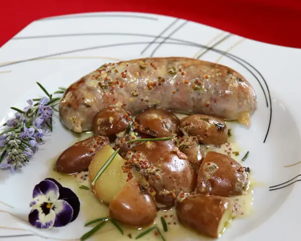 Une andouillette sauce moutarde, accompagnée de pommes de terre grenaille et garnie de romarin et d'une pensée.