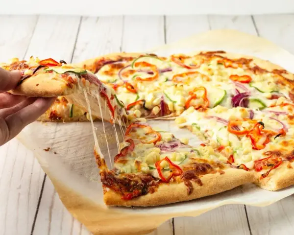 Pyszna pizza domowa z ciągnącym serem, papryką, cebulą i cukinią. Ktoś właśnie podnosi kawałek.