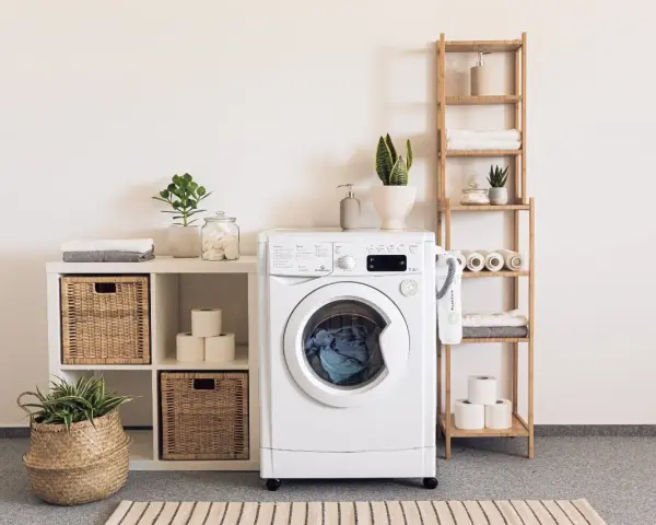Lavadora blanca con cesta de mimbre, plantas y accesorios que se colocan en una prenda.