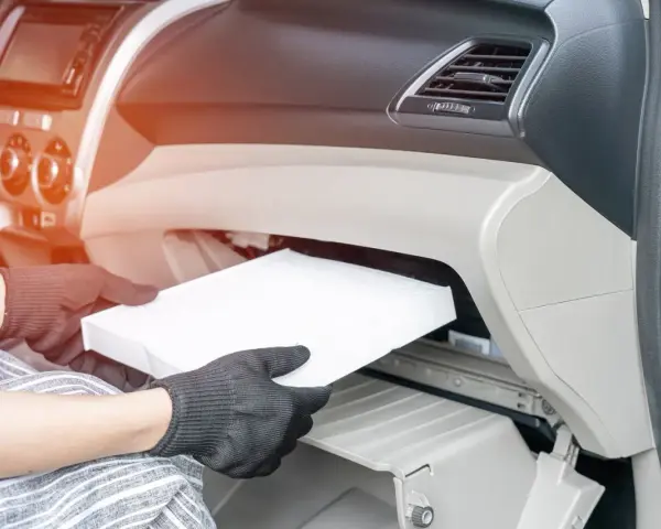 Wymiana filtra kabinowego w Audi A3 8L. Ręce w rękawiczkach wyjmują biały filtr z wnętrza schowka.