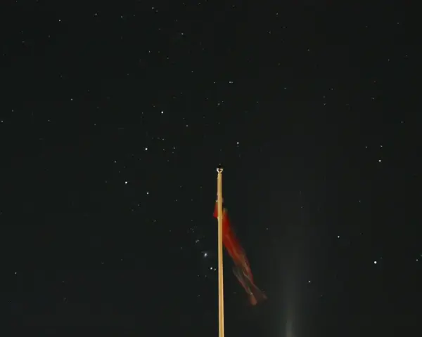 Czerwona flaga na maszcie na tle czarnej, gwieździstej nocy.