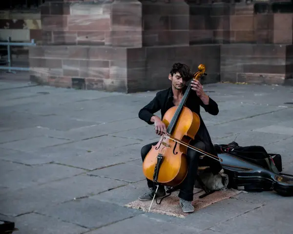 Ein Mann spielt auf einem Cello-Musikinstrument vor einer Steinfassade.