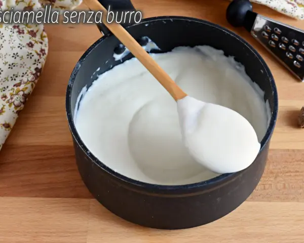 Besciamella senza burro cremosa in pentola, pronta per condire i tuoi piatti. Un cucchiaio di legno la raccoglie.
