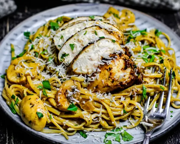 Cremiges Chicken Alfredo mit Pilzen, garniert mit Parmesan und Petersilie. Ein köstliches Gericht, das Lust auf mehr macht.