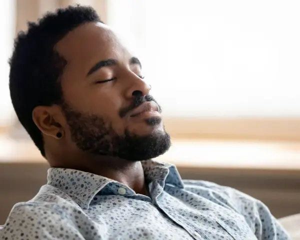 A man with closed eyes and a beard breathes deeply, finding a moment to ground himself amidst the day's chaos.