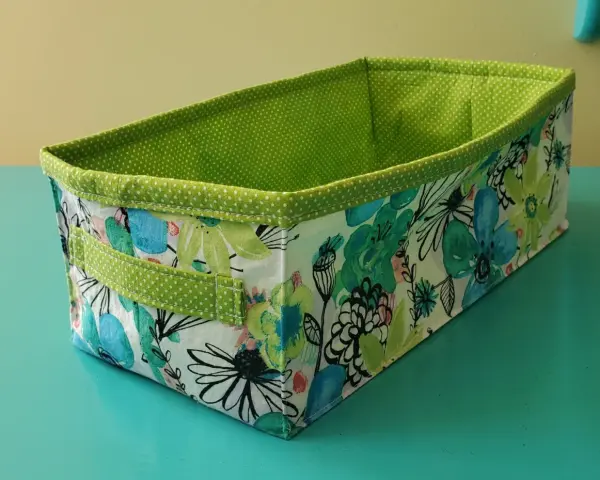 Panier rectangulaire en tissu, doublé de pois verts. Son extérieur est orné d'un motif floral coloré, parfait pour ranger vos affaires avec style.