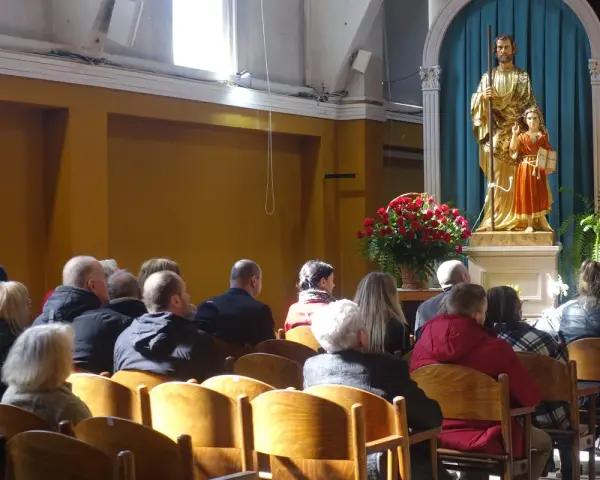 Ludzie w kościele, przed ołtarzem z figurą św. Józefa i Dzieciątka Jezus. W tle bukiet czerwonych róż. Sanktuarium Matki Bożej Częstochowskiej.