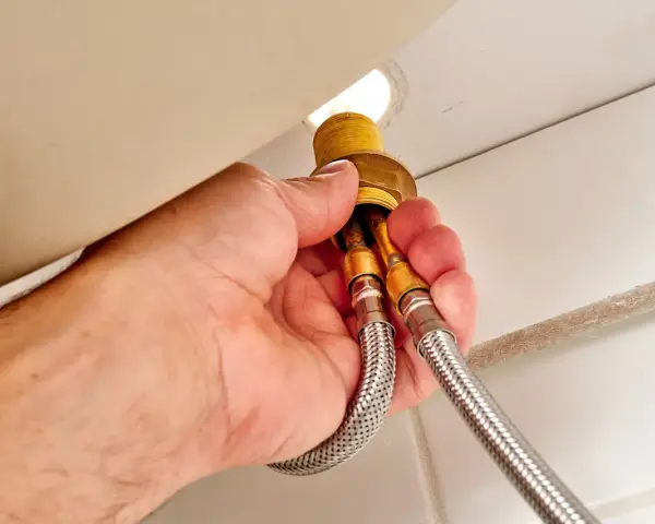 Hands disconnect braided water supply lines from a faucet base, a key step in how to remove kitchen faucet.