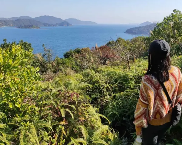 Frauen genießen die Aussicht beim Hong Kong Hiking. Grüne Vegetation und das blaue Meer erstrecken sich bis zu den Hügeln.