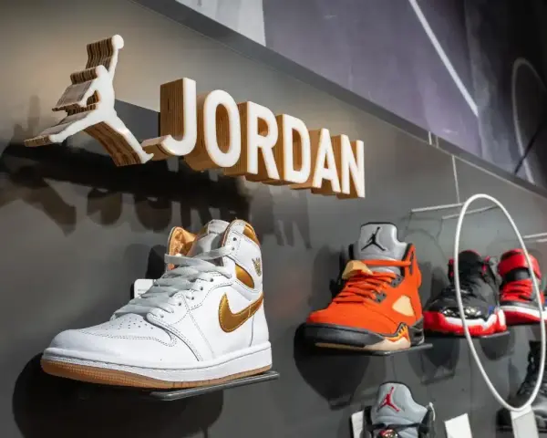 Na wystawie butów Jordan, białe Air Jordan 1 z złotymi akcentami. Obok pomarańczowe Air Jordan 5. Czy 8 5 jaki to rozmiar buta?