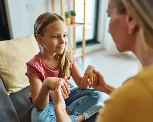 Mama spokojnie tłumaczy córce, jak rozmawiać z dzieckiem o złym zachowaniu. Dziecko słucha uważnie, trzymając dłonie mamy.
