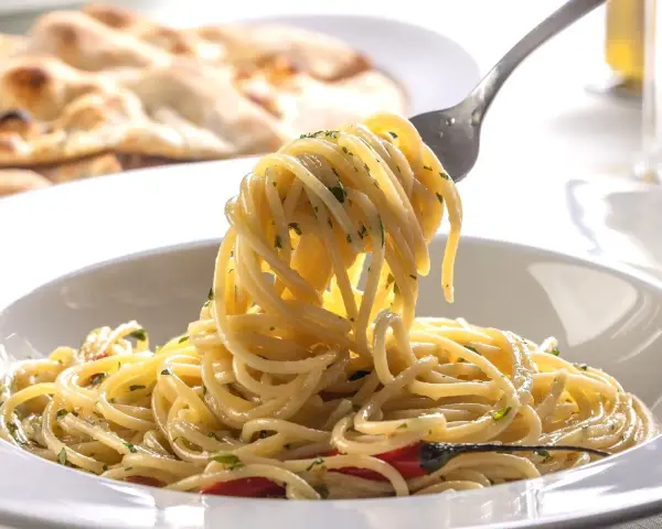 Porcja spaghetti z ziołami na widelcu, w tle płaski chleb.