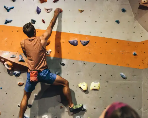 Mężczyzna wspina się po ścianie z kolorowymi chwytami. To właśnie bouldering – wspinaczka bez liny na niskich ściankach.