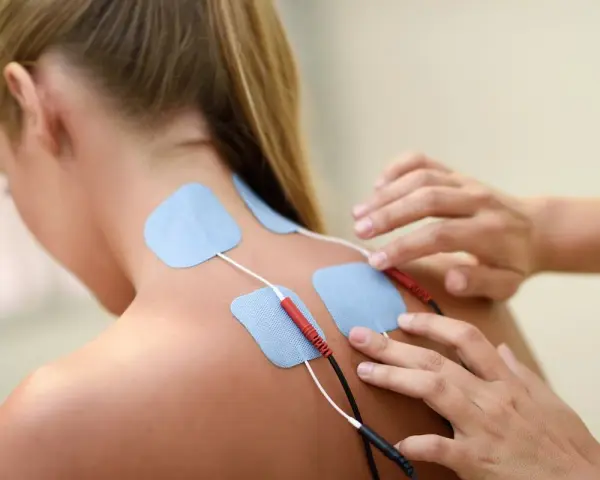 Elektrody na plecach kobiety podczas terapii fizykalnej. Terapeuta przygotowuje do zabiegu.