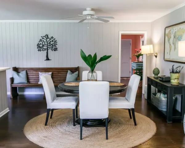 Elegante decoracion comedor pequeño con mesa redonda, sillas blancas, banco de madera y arte de árbol en la pared.