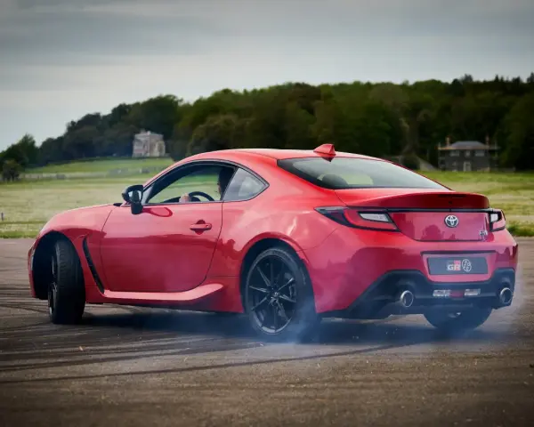 Czerwona Toyota 86 GR w poślizgu, z opon dymiących na asfalcie. W tle zielone pola i drzewa.