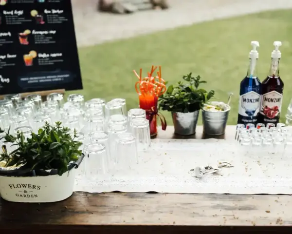 Stół z kieliszkami, butelkami syropów i miętą, gotowy na przygotowanie drinków na wesele. Przepisy na drinki są widoczne na tablicy w tle.
