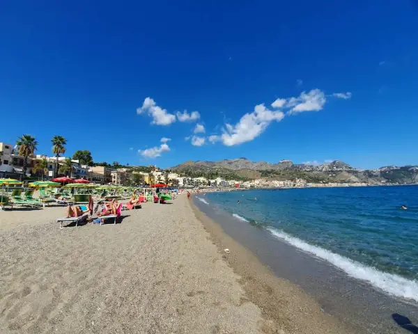 Spiaggia affollata a Giardini di Naxos, con lettini, ombrelloni e persone che si rilassano sotto il sole siciliano.