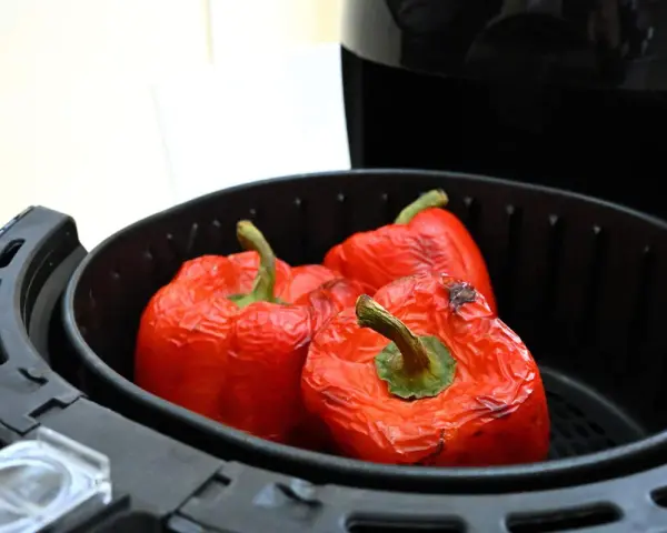 Tre peperoni rossi interi, leggermente abbrustoliti, pronti per essere cucinati nella friggitrice ad aria.