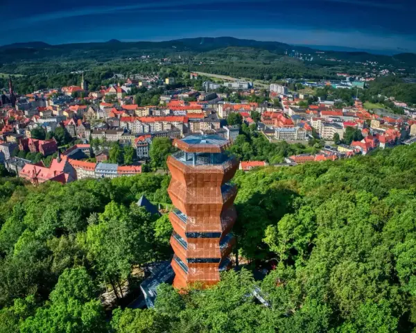 Nowoczesna wieża widokowa w otoczeniu zieleni, z panoramą miasta Wałbrzych i Sudetów Wałbrzyskich w tle.