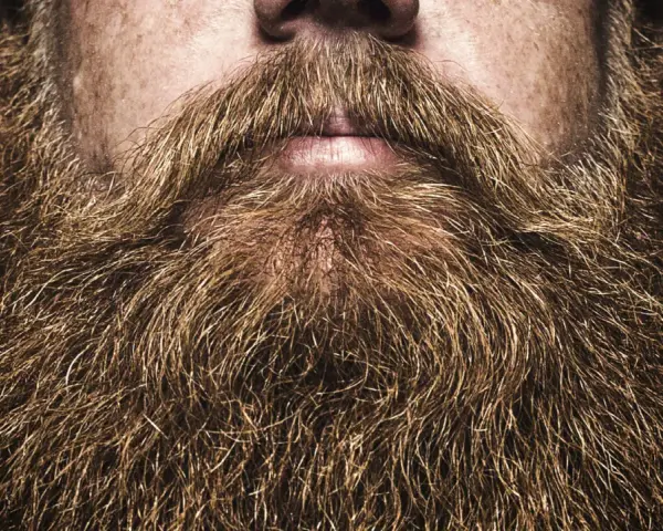 Primer plano de unas barbas hipster voluminosas y doradas, con un bigote tupido sobre unos labios entreabiertos.