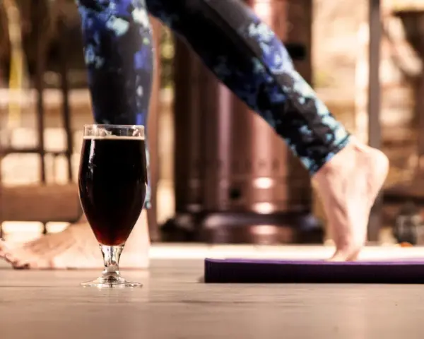 Kreatyna a alkohol: czy można połączyć trening z piwem? Nogi w legginsach i szklanka ciemnego piwa na pierwszym planie.