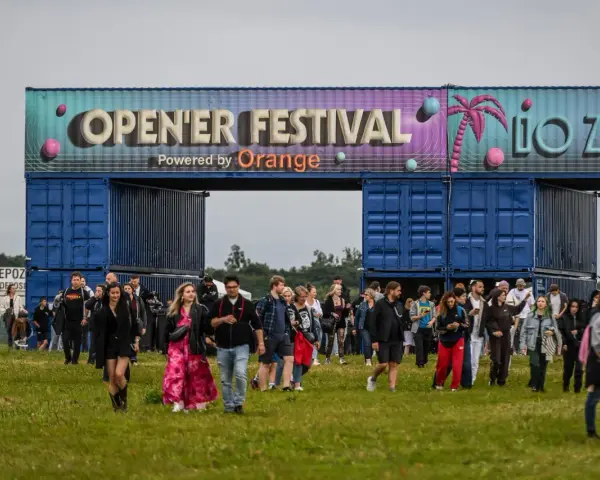 Tłum ludzi wchodzi na teren festiwalu. Nad nimi brama z napisem "OPEN'ER FESTIVAL". Kto będzie następny?