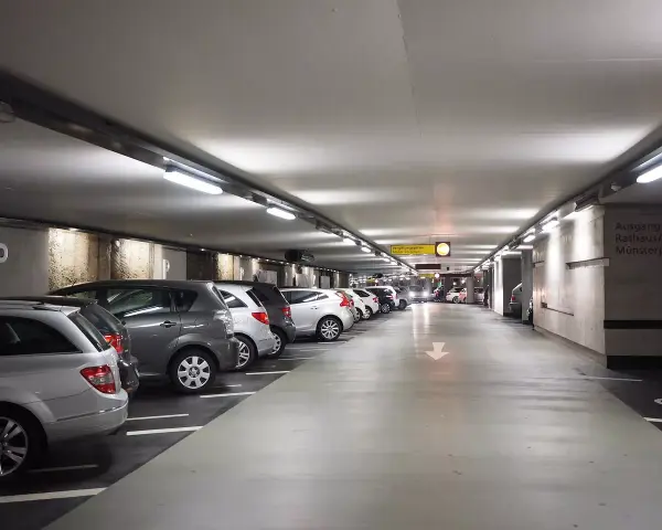 Podziemny parking z rzędami samochodów. Dostępny jest wynajem miejsca parkingowego.