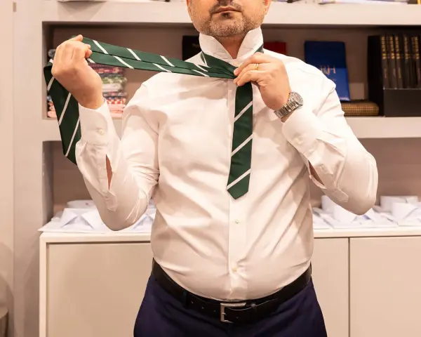 Uomo in camicia bianca che impara come fare il nodo alla cravatta verde a righe.