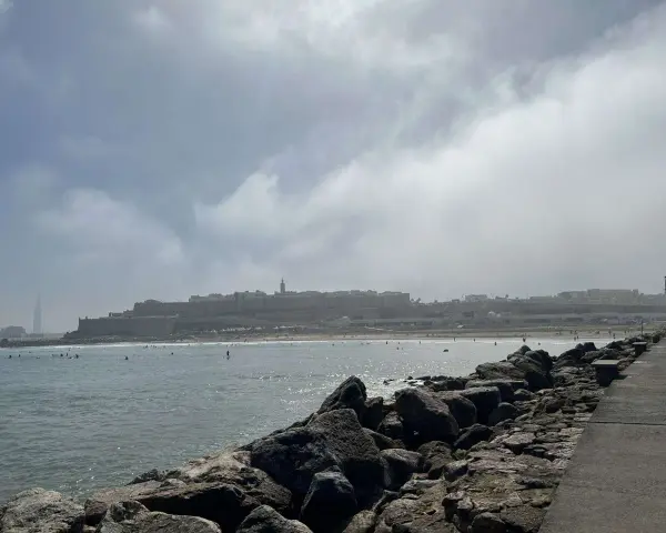 Spokojna plaża z surferami i miastem w tle. Czy Maroko jest bezpiecznym krajem? Widok sugeruje, że tak, ludzie cieszą się słońcem i morzem.
