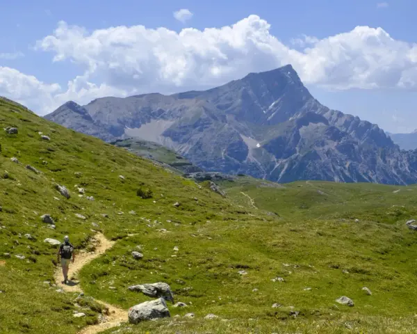 Escursionista su sentiero erboso, con imponente gruppo montuoso delle Dolomiti sullo sfondo.