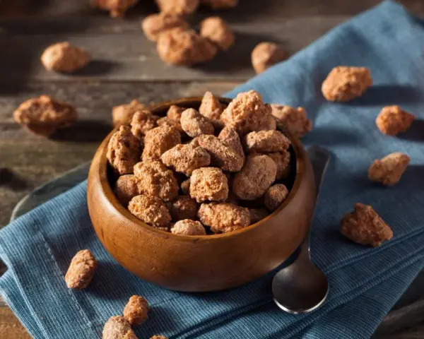 Schüssel mit gebrannten Mandeln, Zimtstangen und Löffel. Ein süßer Snack, der auch in der Schwangerschaft genossen werden kann.