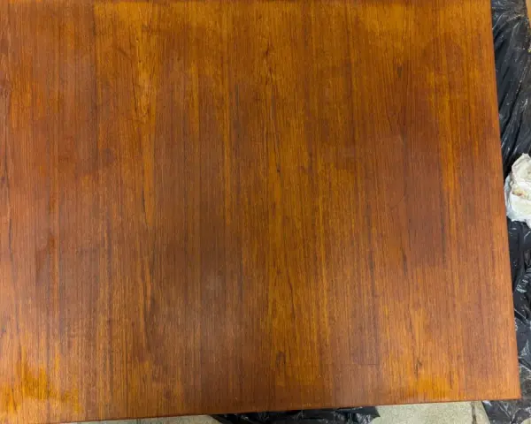 Förbereder för att slipa teakbord. En bit teak ligger på svart plast, bredvid en slipmaskin och en trasa.