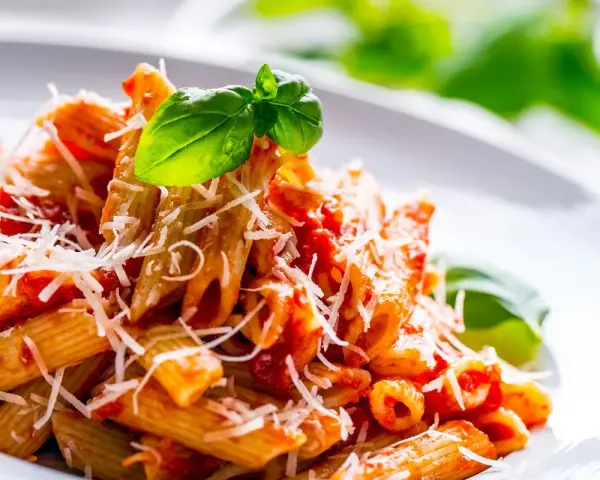 Penne al pomodoro con basilico fresco e parmigiano grattugiato, un classico tra i sughi per pasta.