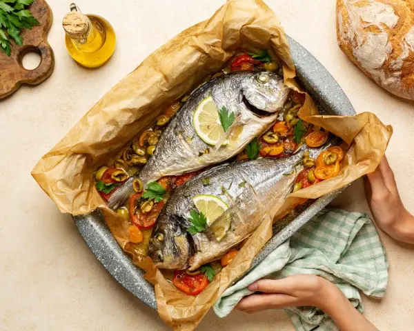 Due agoni in carpione cotti al forno con pomodorini, olive e limone, pronti per essere gustati.